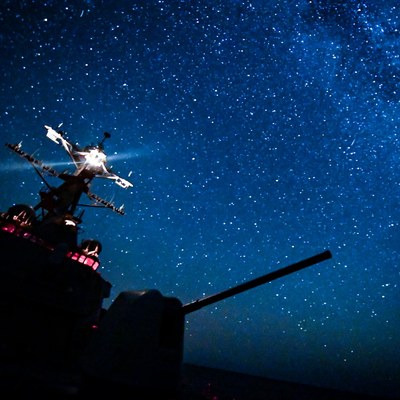 A U.S. Navy destroyer's gun mount silhouetted at night under the Milky Way.